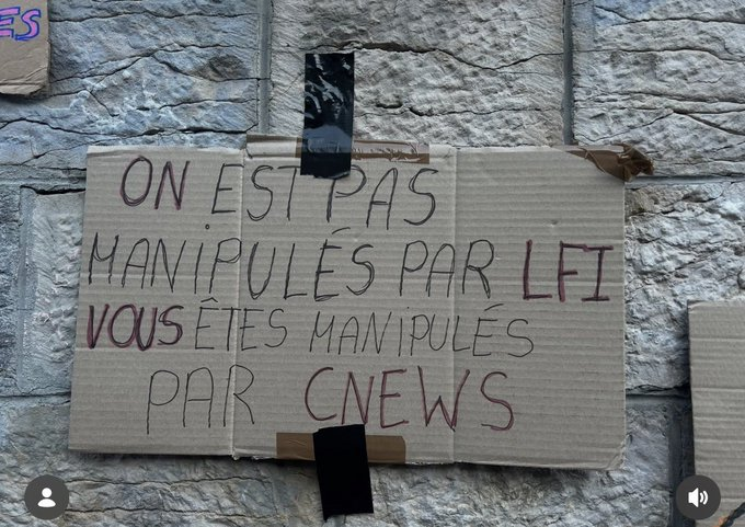 Pancarte en carton fixée sur un mur en pierre, avec l'inscription manuscrite : « On est pas manipulés par LFI, vous êtes manipulés par CNEWS ».